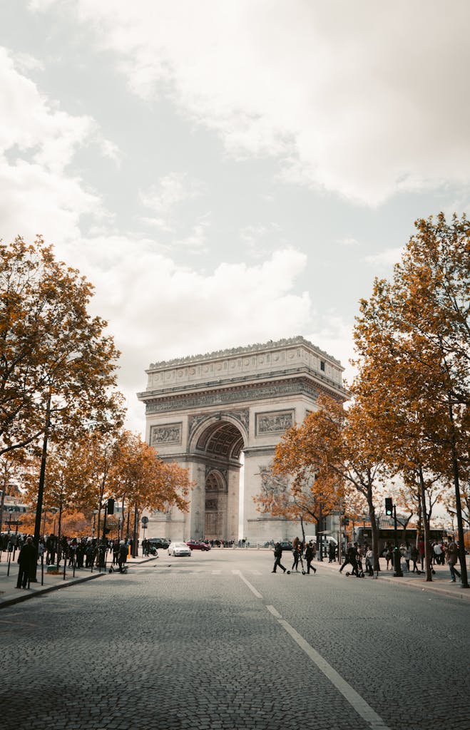 A classic view of the Arc de Triomphe in Paris, surrounded by autumn foliage.