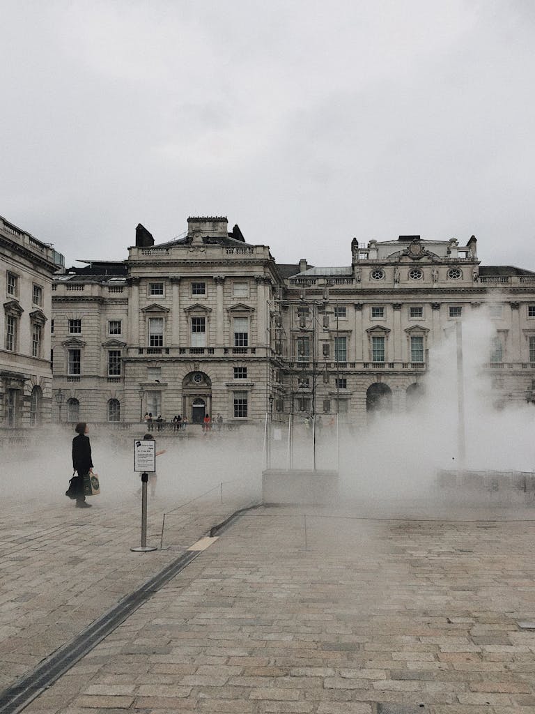 A person walks past Somerset House in London, enveloped in atmospheric fog creating a mysterious ambiance.