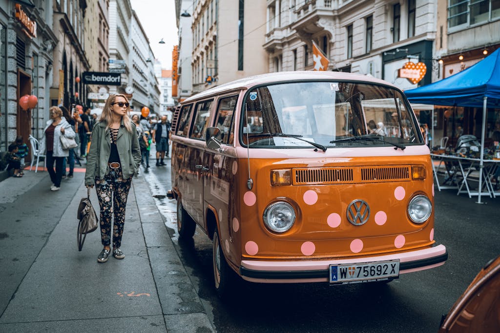 A vibrant street scene in Vienna featuring a classic orange Volkswagen van and pedestrians.