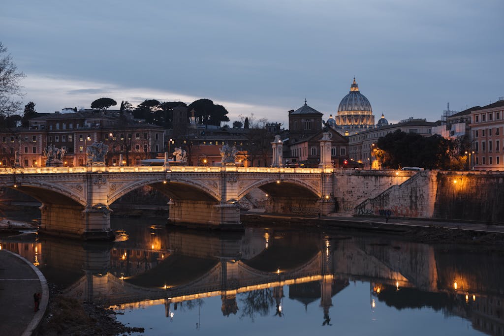 Beautiful evening view of St. Peter's Basilica and a bridge reflection in Rome's Tiber River.