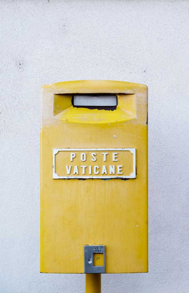 Bright yellow Vatican City mailbox against a blank wall, showcasing international mail service.