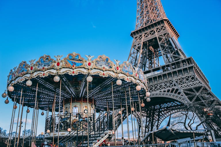 Eiffel Tower with a classic carousel in foreground on a bright day in Paris, France.