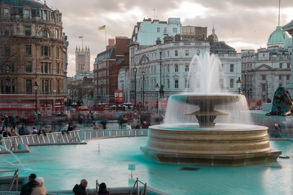 Long exposure photo of the iconic Trafalgar Square fountain with blurred crowd in London, England.