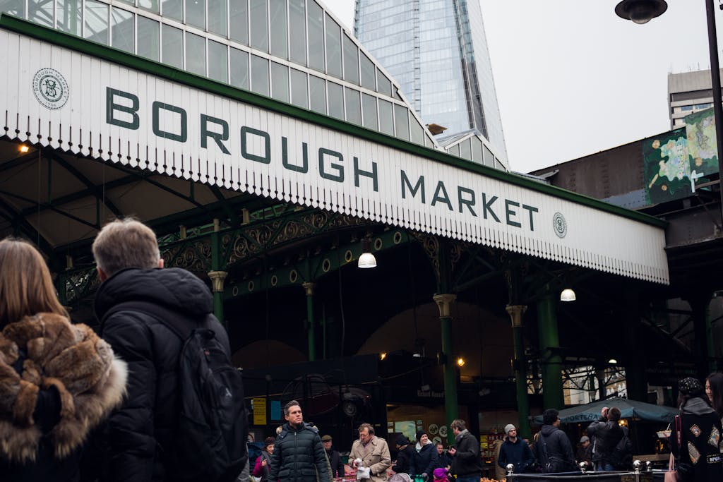 People enjoying a bustling day at London's iconic Borough Market with city skyscrapers in the background.