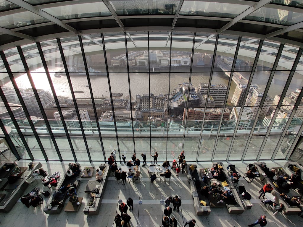 People inside a modern atrium with views of London's skyline and river during daytime.