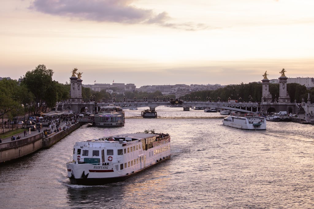 Scenic sunset view of the Pont Alexandre III over the Seine River with boats and vibrant Paris skyline.