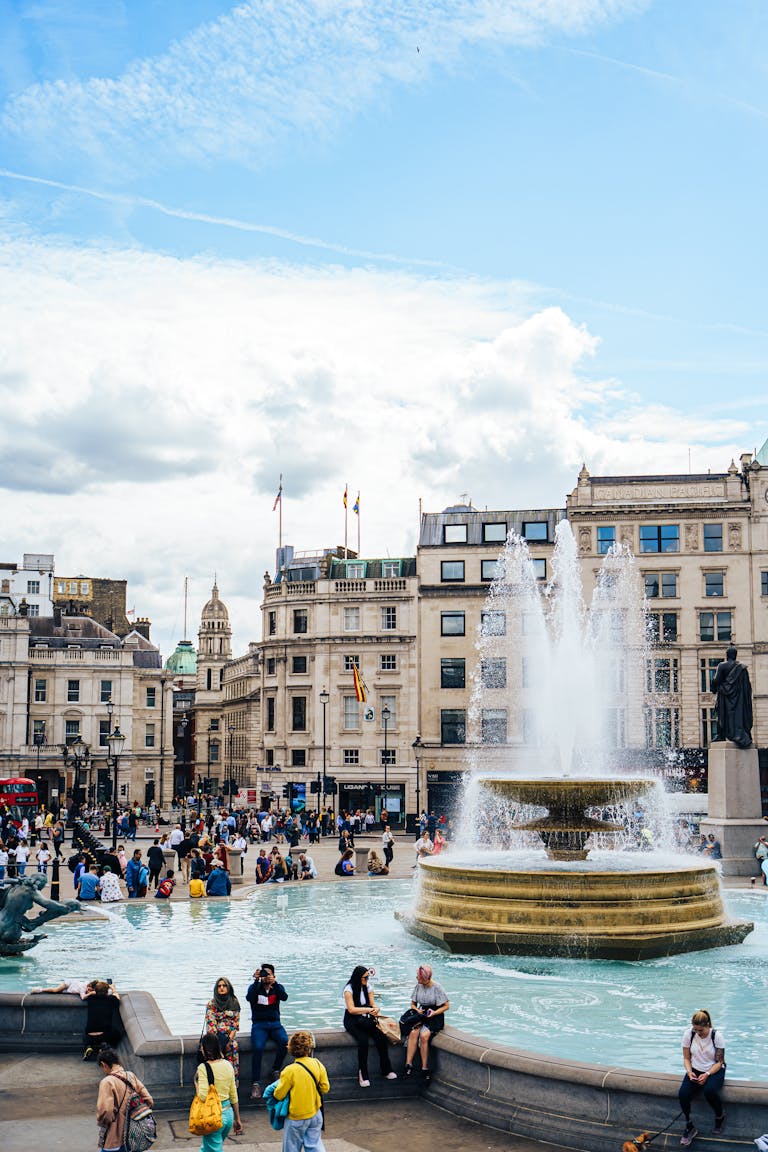 Vibrant scene at London's Trafalgar Square with a fountain and lively crowd on a sunny summer day.